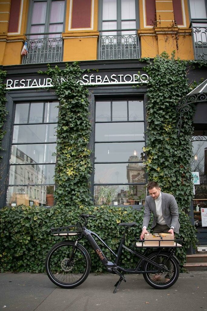 A man loading an electric cargo bike in front of a store covered with leaves